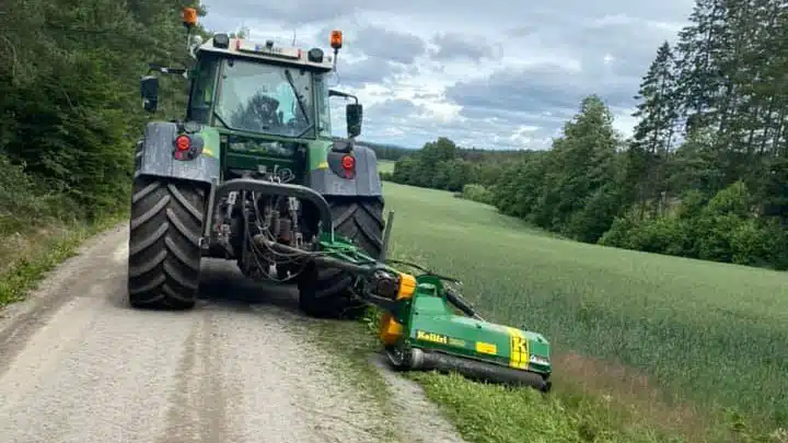Traktor med kantklipper på landevei som klipper kantgresset
